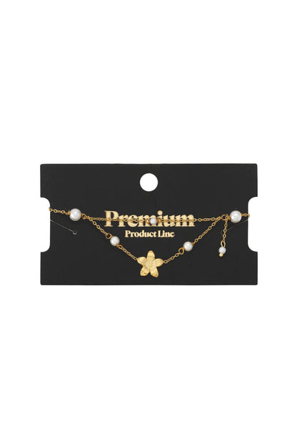 Layered gold chain bracelet featuring a delicate floral charm and white pearl accents on a black display card.