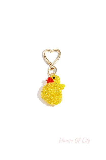 Close-up of a beaded yellow duck charm with orange beak attached to a gold heart-shaped clasp.
