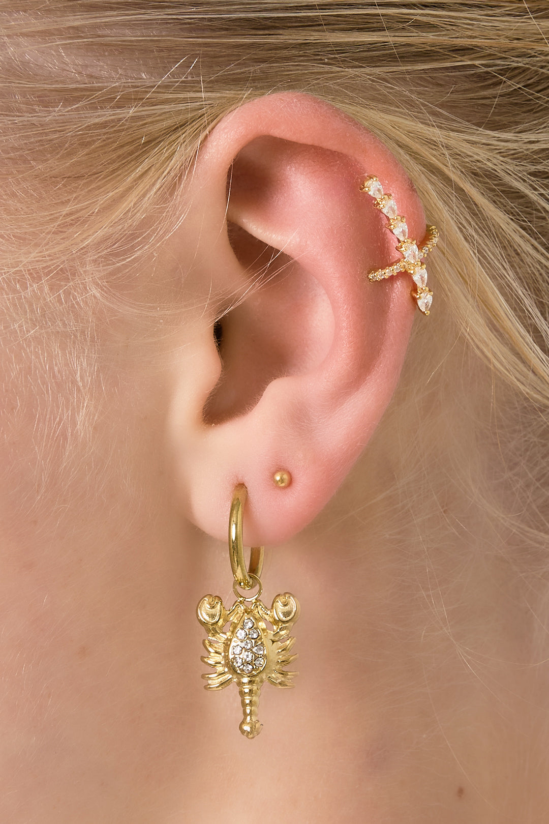 Close up of a woman wearing the gold Scorpio charm hoop earring on her ear paired with additional gold ear cuffs