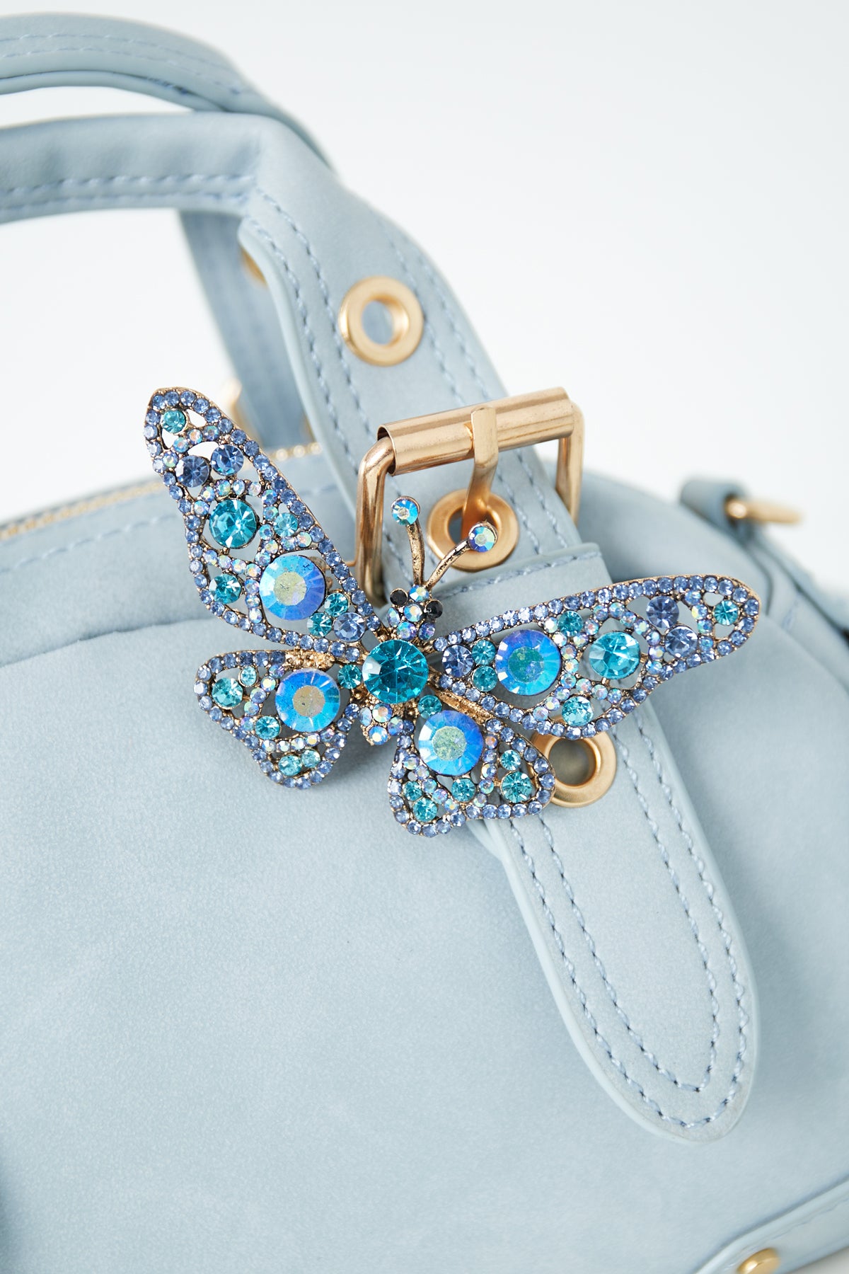 Blue rhinestone butterfly brooch pinned to a light blue handbag strap with gold buckle hardware