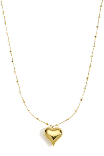 Gold long necklace with polished heart pendant and small bead details on chain, displayed on white background