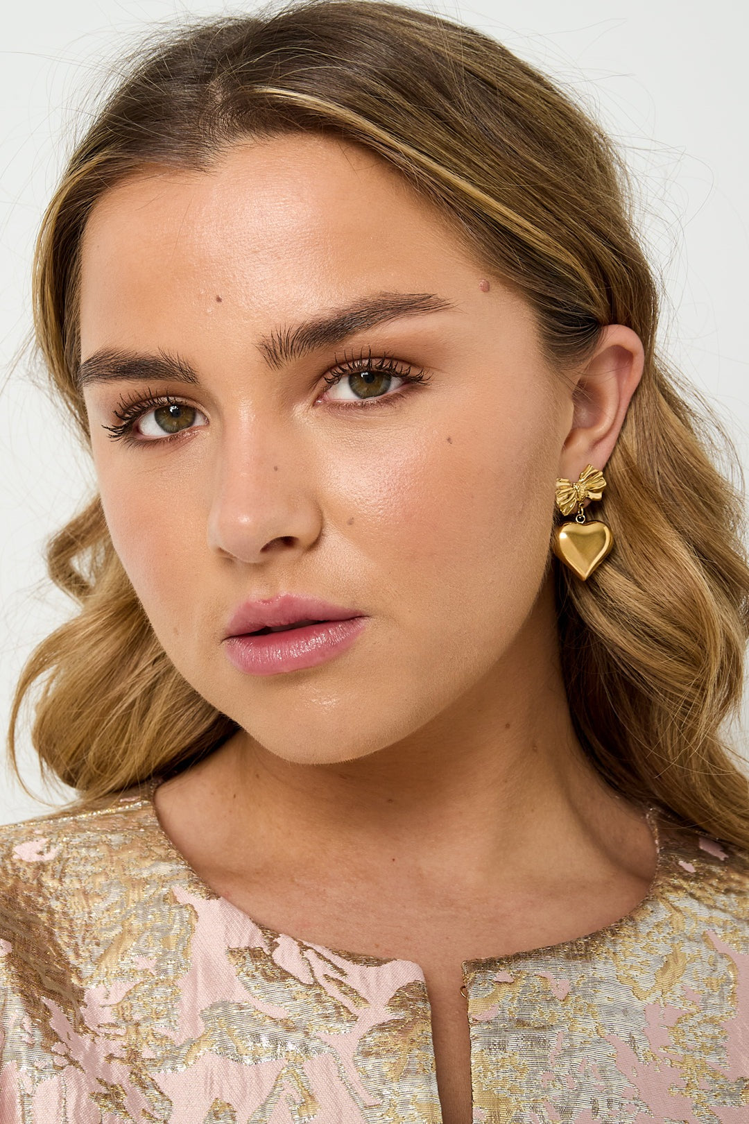 Model wearing the gold bow and heart drop earrings styled with a pink and gold patterned top