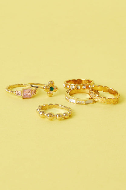 Collection of six gold rings with varied designs including gemstone accents and textured bands on a yellow background