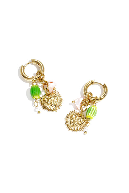 Pair of gold-tone hoop earrings each adorned with a spiked heart pendant, green ribbed bead, pink glaze stone, and small pearl on white background