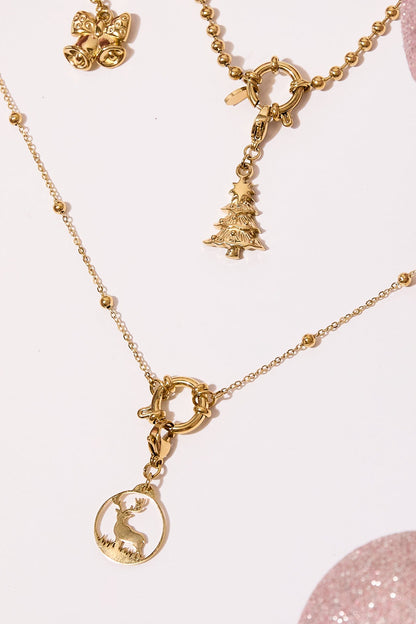 Flat lay of a gold-tone necklace featuring reindeer and Christmas tree charms against light pink surface