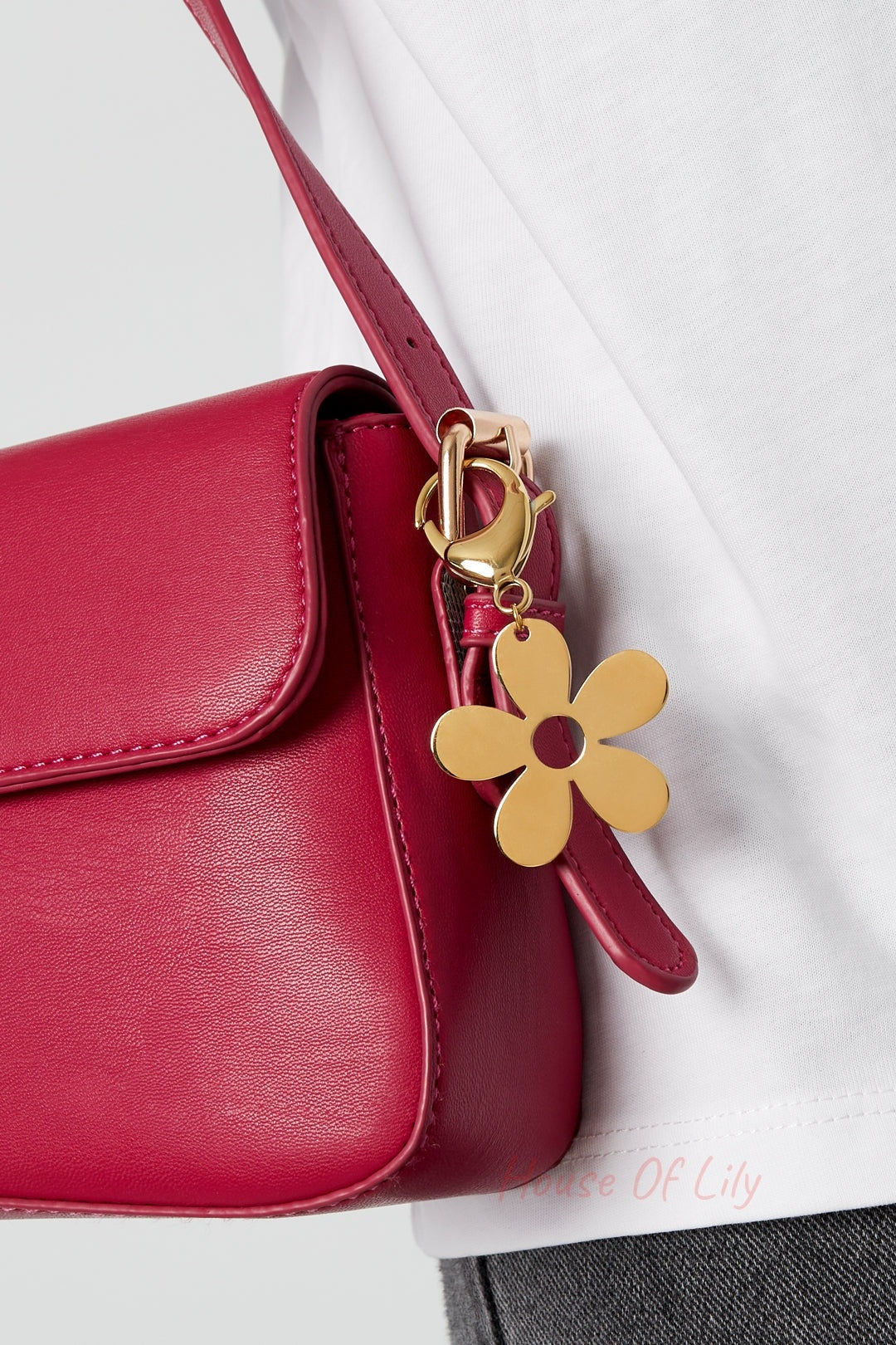 Gold flower charm clipped to the strap of a red handbag worn by a person in a white shirt and jeans