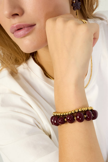 Woman wearing burgundy marbled beaded stretch bracelet stacked with gold bead bracelets on wrist