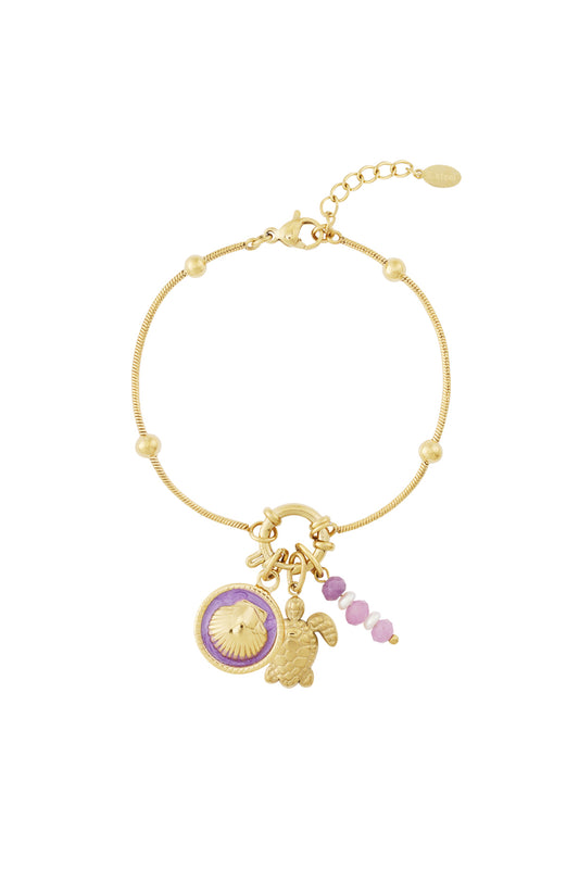 Gold charm bracelet with turtle, shell, and pink bead charms hanging together on a white background