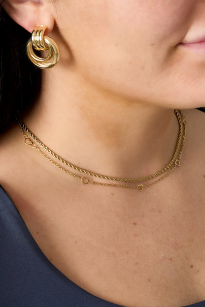 Close-up of woman wearing the gold heart chain necklace layered with other necklaces and gold hoop earrings