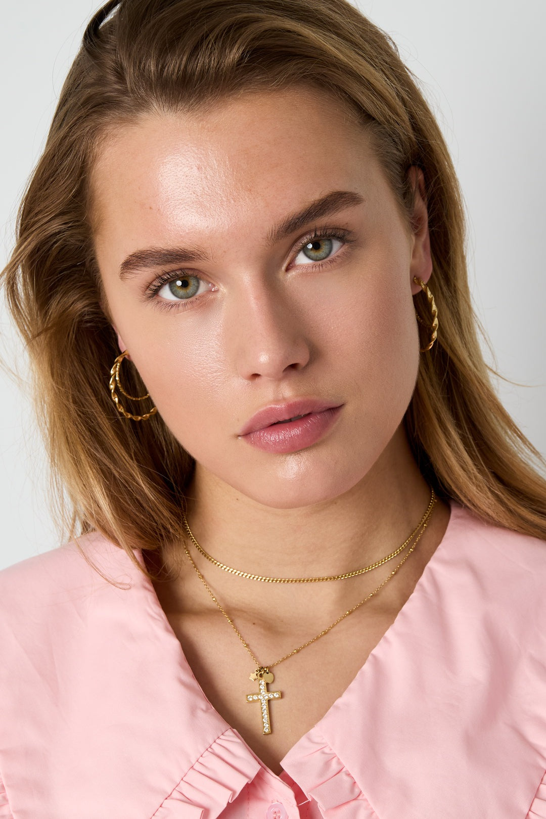 Iconic Y2K gold cross necklace with crystal pavé on a delicate chain worn by a woman with gold hoop earrings.