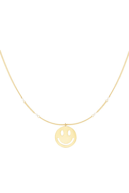 Close-up of gold chain necklace featuring a smiling face cut-out pendant and small pearl accents on the chain