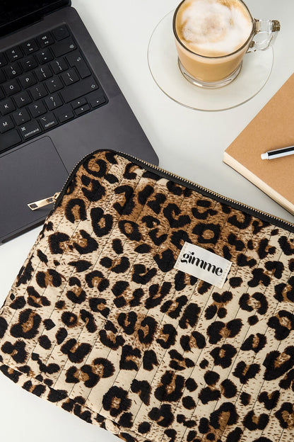 Close-up of leopard print laptop sleeve next to laptop, coffee, and notebook on desk