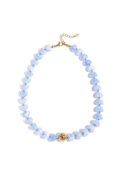 Close-up image of a blue variant of the heart-shaped beaded necklace with gold round bead and adjustable clasp on white background