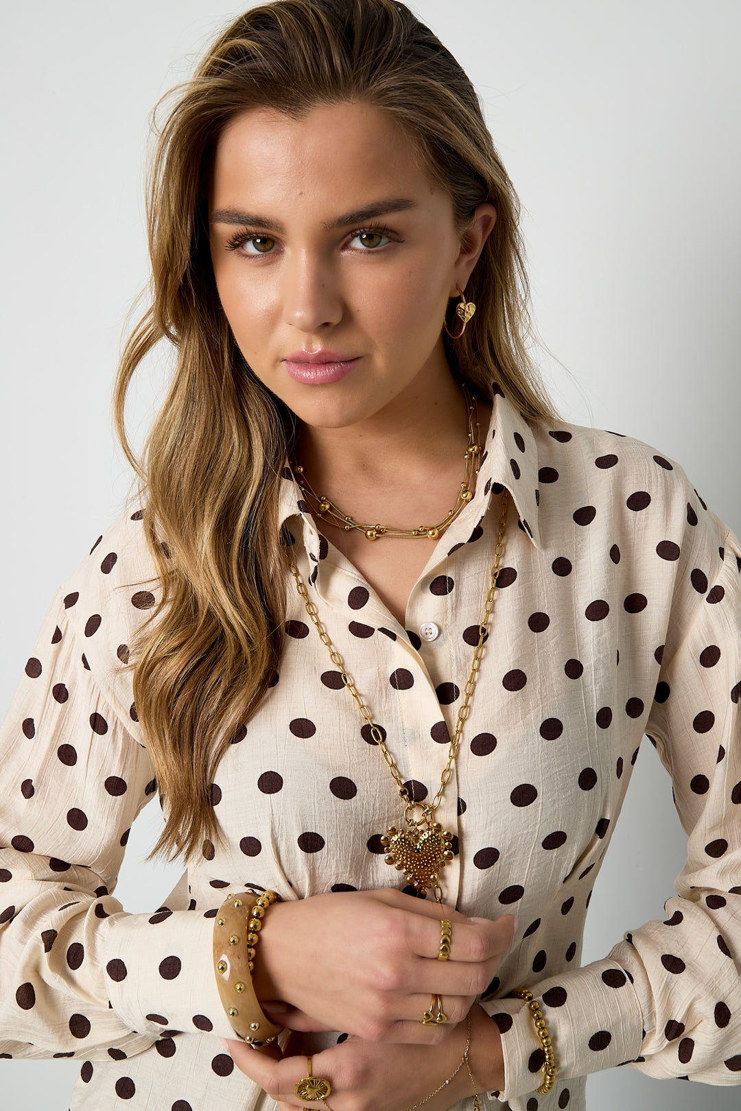 Woman styling multiple gold bracelets, rings, and layered necklaces on polka dot shirt