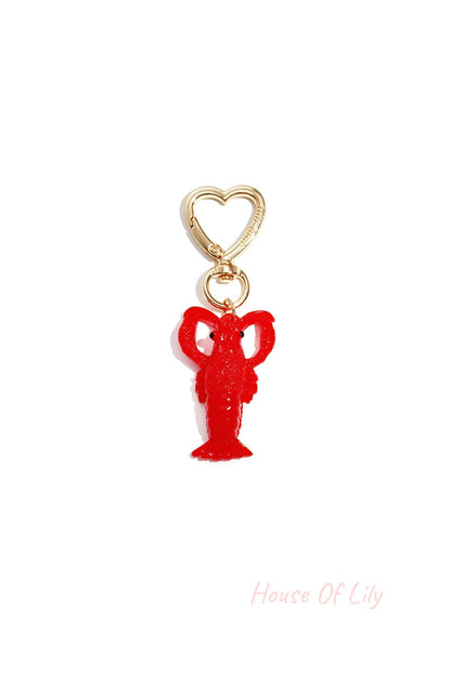 Bright red resin lobster bag charm with shiny gold heart-shaped clip hardware on white background