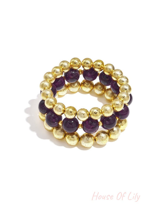 Set of three beaded bracelets with purple marbled beads and textured gold spheres on white background