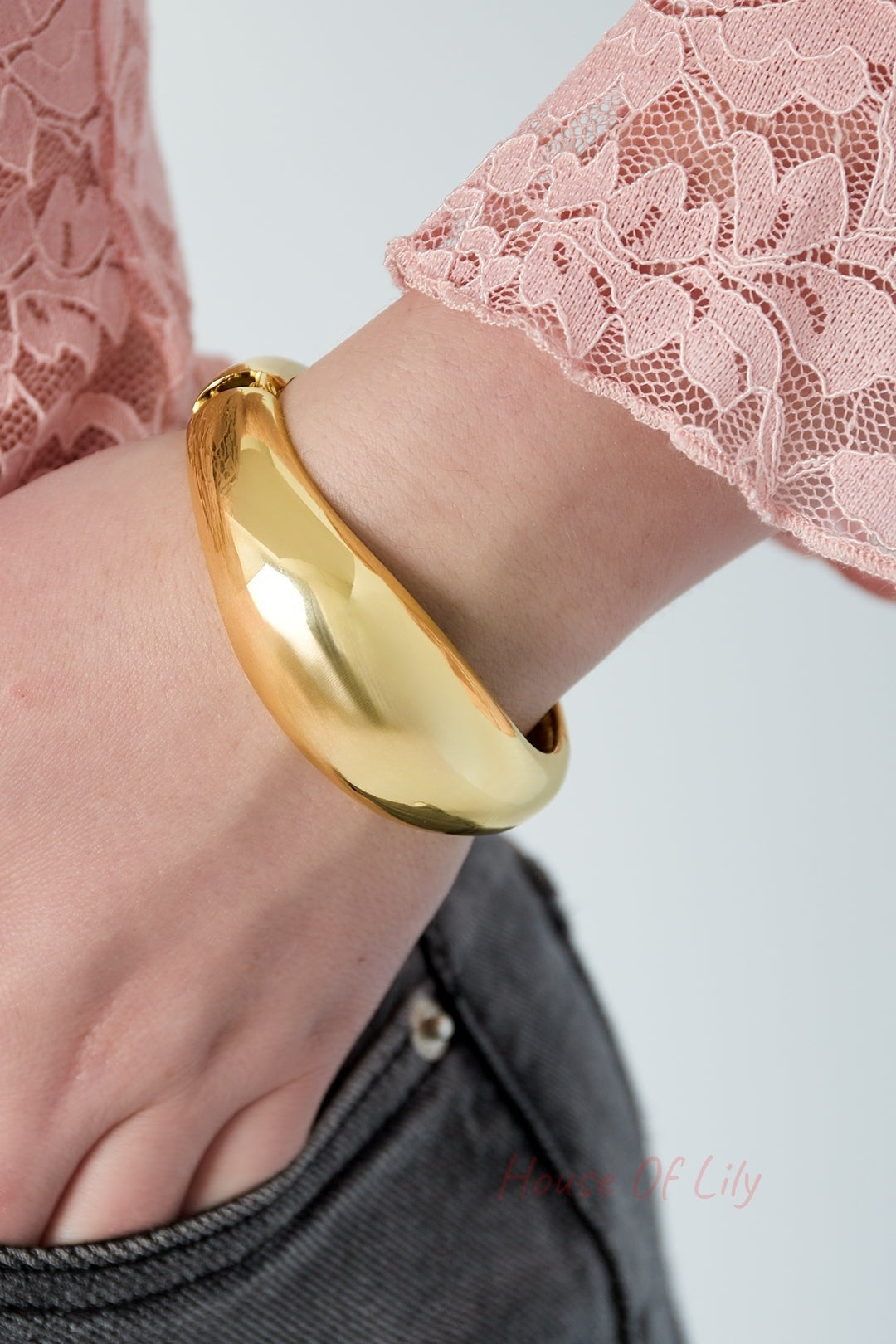 Close-up of gold dome-shaped bangle bracelet worn on wrist with pink lace sleeve and denim