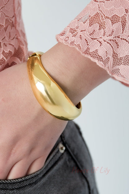 Close-up of gold dome-shaped bangle bracelet worn on wrist with pink lace sleeve and denim