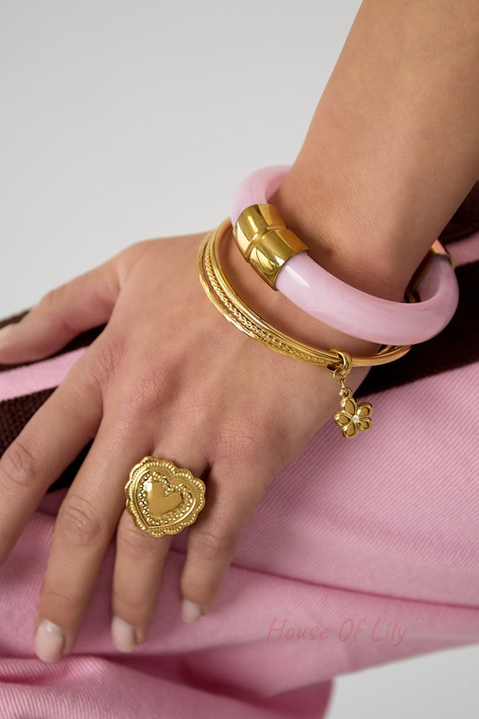 Woman's wrist wearing gold bangles with flower charm alongside pink bangle and gold heart ring