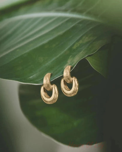 Textured gold drop earrings rest on a large green leaf.