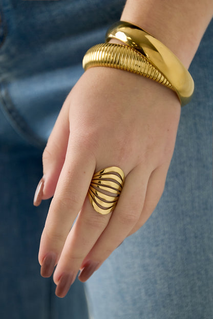Close-up of a woman wearing the gold sculptural wave statement ring paired with two chunky gold bracelets and denim