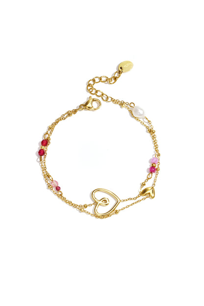 Gold-tone double chain bracelet with open heart charm, small solid heart charm, pink and red beads, and a pearl accent on a white background