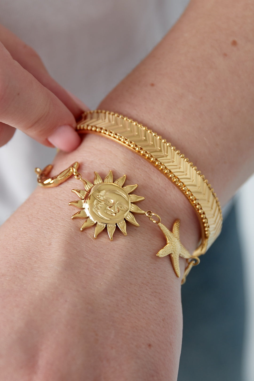 Close-up of gold celestial charm bracelet worn on wrist alongside textured gold bangles, showing details of sun and star charms