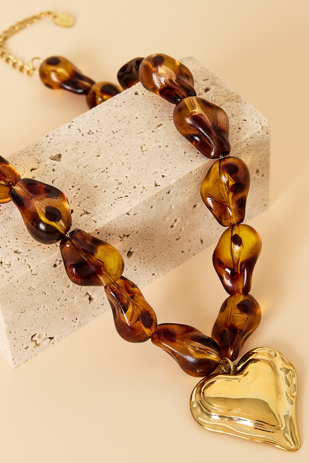 Close-up detail of amber acrylic beads and gold heart pendant resting on beige textured surface