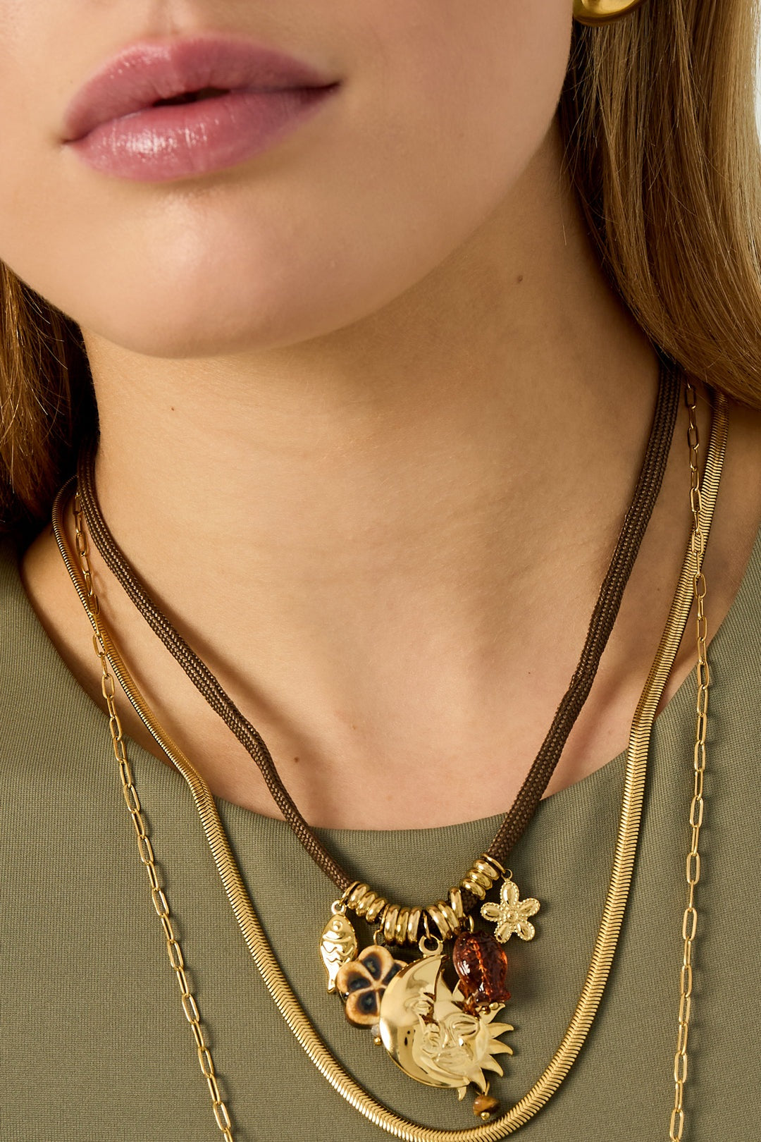 Close-up of model's neck showcasing detailed charms on the brown rope pendant necklace layered with gold chains