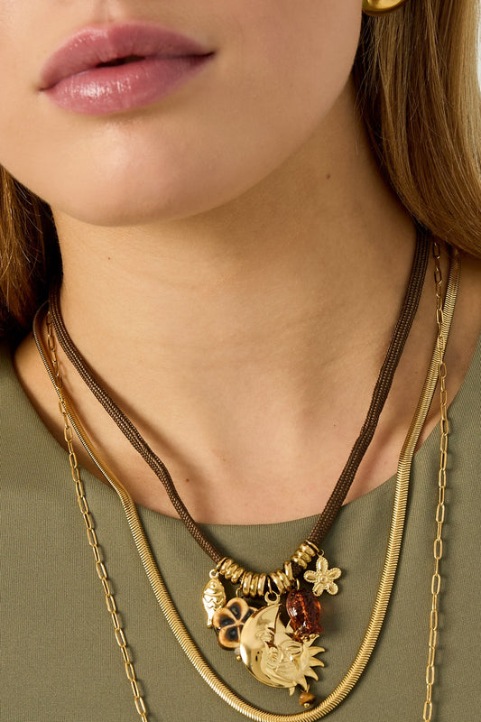 Close-up of model's neck showcasing detailed charms on the brown rope pendant necklace layered with gold chains
