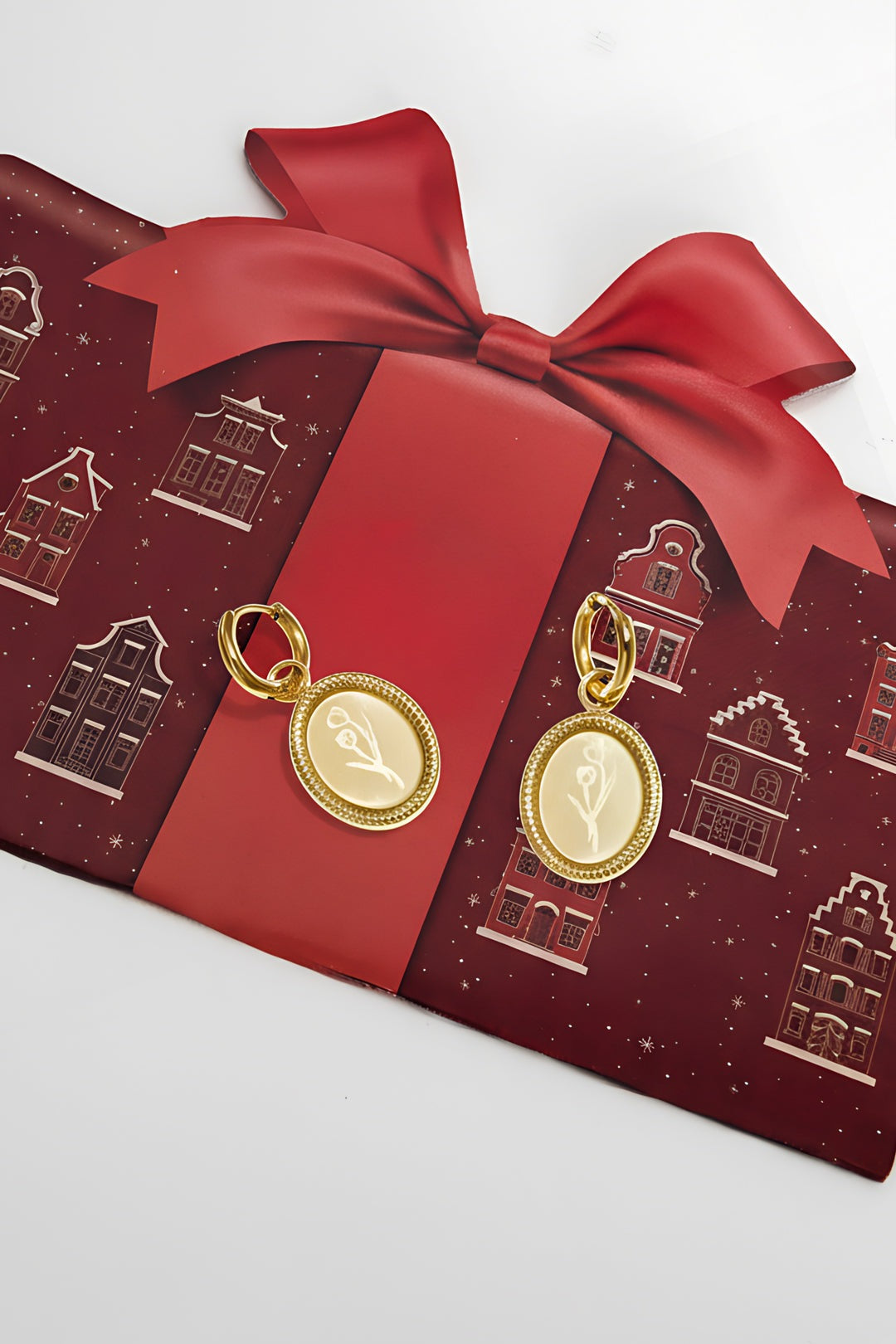 Gold floral oval hoop earrings on red gift wrap with large ribbon bow