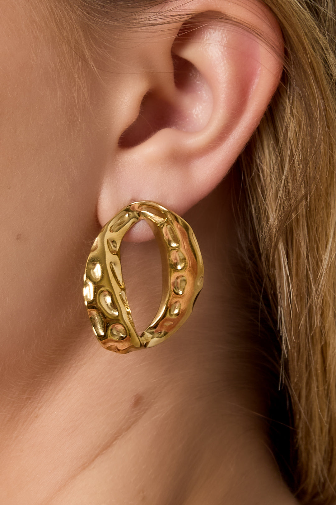 Model wearing textured gold-tone oval stud earring showcasing its unique shape and soft reflective surface.