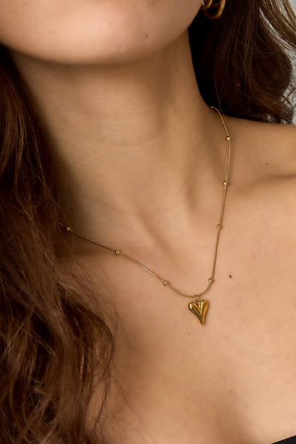 Close detail of the gold heart pendant necklace on a model’s neck showcasing the smooth sculptural pendant and glossy chain