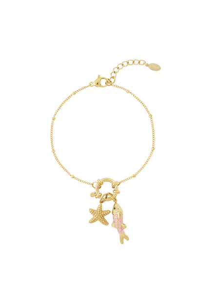 Gold charm bracelet styled with starfish and pink-enamel fish charms attached, lobster clasp and extender chain visible