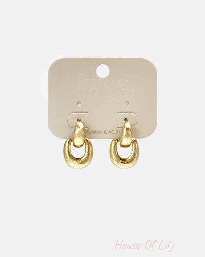A pair of brushed gold drop earrings mounted on a beige card display.