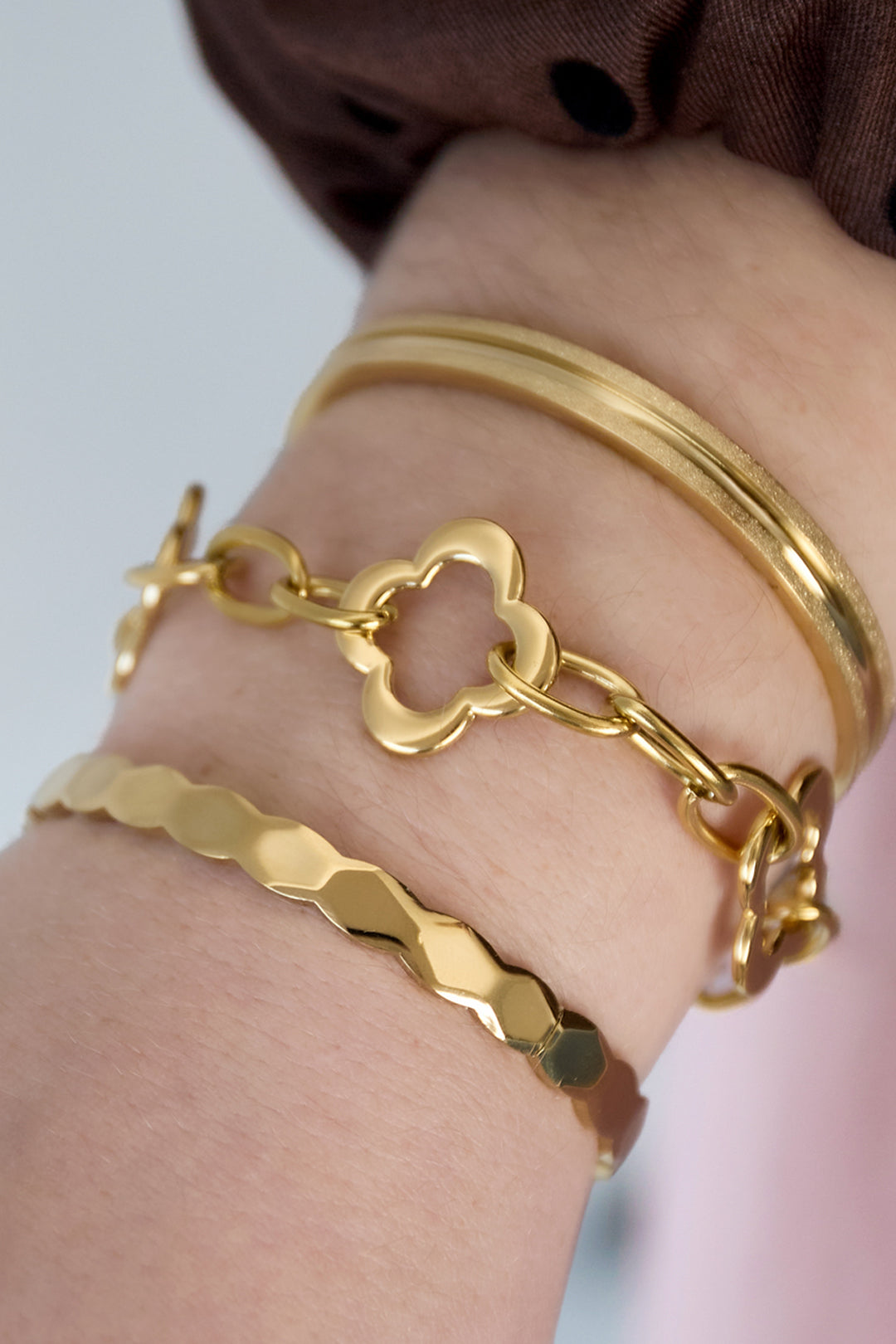 Close-up of wrist wearing gold clover chain bracelet paired with other gold bangles