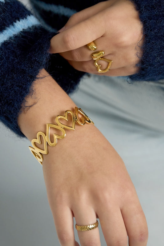 Woman wearing gold-tone linked heart open cuff bracelet and coordinating rings with blue fuzzy sweater