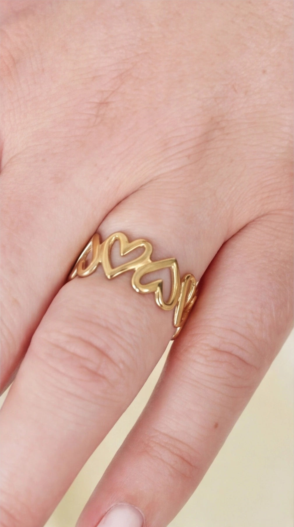 Gold heart-shaped ring on a finger with a plain background
