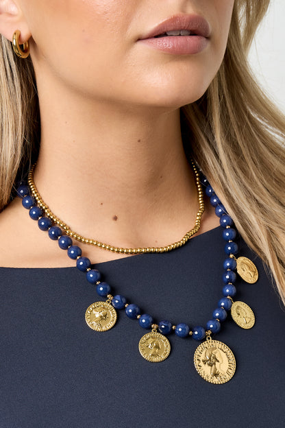Close-up of navy blue beaded necklace with gold-tone coin pendants worn by woman in navy top