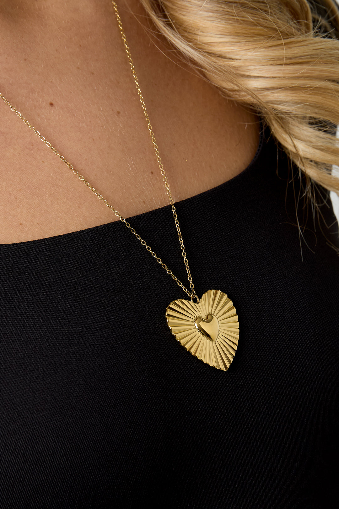 Detailed close-up of the gold heart pendant necklace worn by model, showing sunburst texture and polished heart center