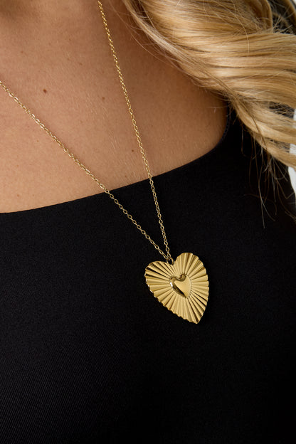 Detailed close-up of the gold heart pendant necklace worn by model, showing sunburst texture and polished heart center