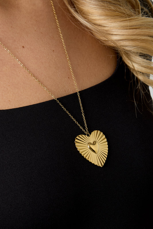 Detailed close-up of the gold heart pendant necklace worn by model, showing sunburst texture and polished heart center
