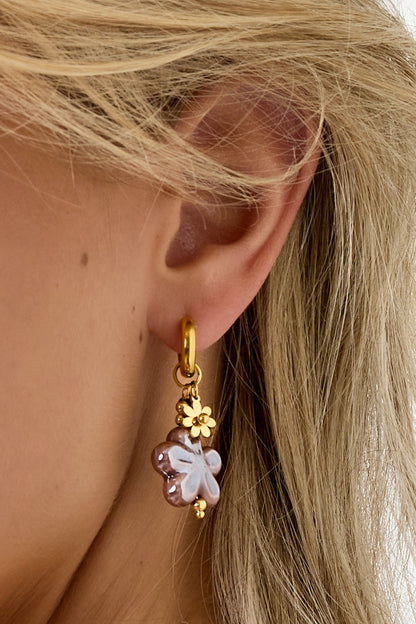 Close side view of earring featuring a mauve-lilac flower resin charm with gold flower detail, worn by a woman