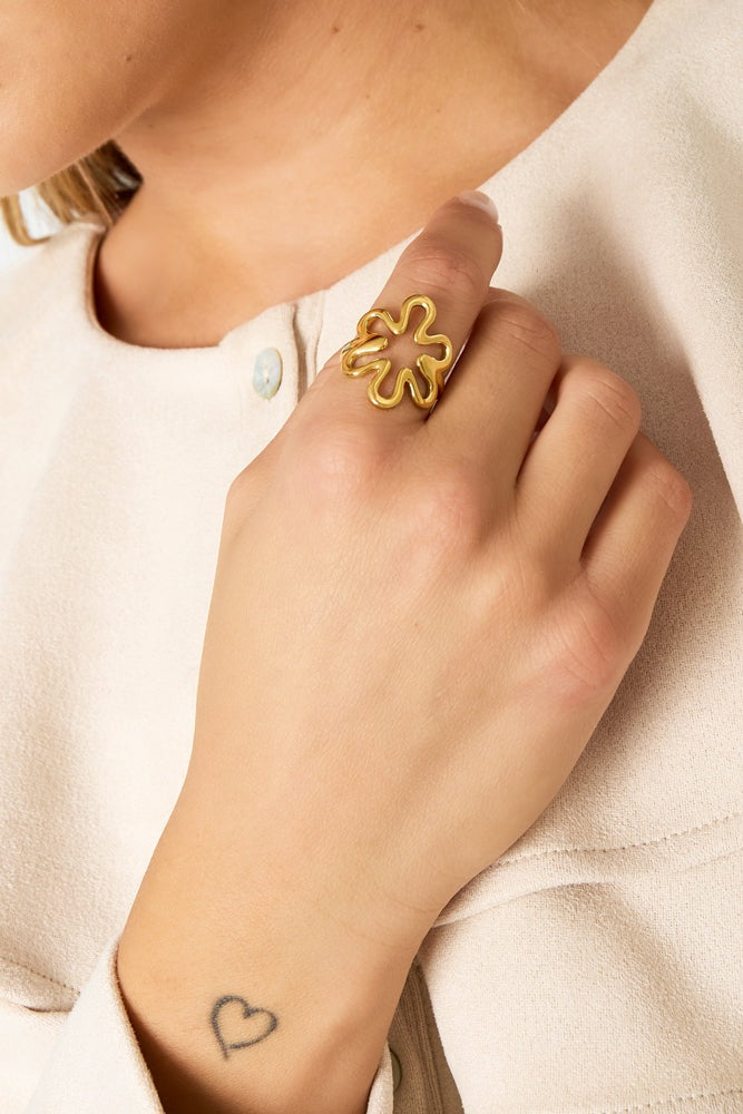 Hand wearing gold floral outline adjustable ring with cream blouse sleeve and heart tattoo on wrist