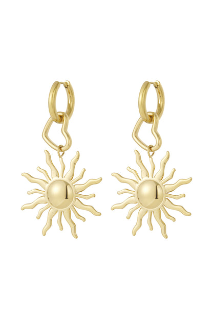 Pair of gold tone drop earrings with sun-shaped pendants and heart-shaped links attached to small gold hoops