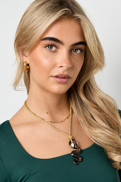 Portrait of woman modeling the snake pendant necklace, styled with gold hoop earrings and blonde hair against neutral background