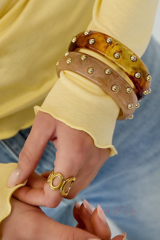 Two studded resin bangles in brown and pink colors worn on wrist with yellow sleeve