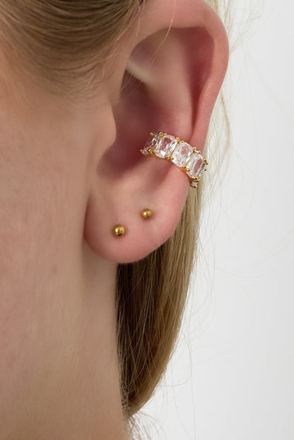 Model wearing gold sparkling stone ear cuff on upper ear with two small gold stud earrings on lower ear