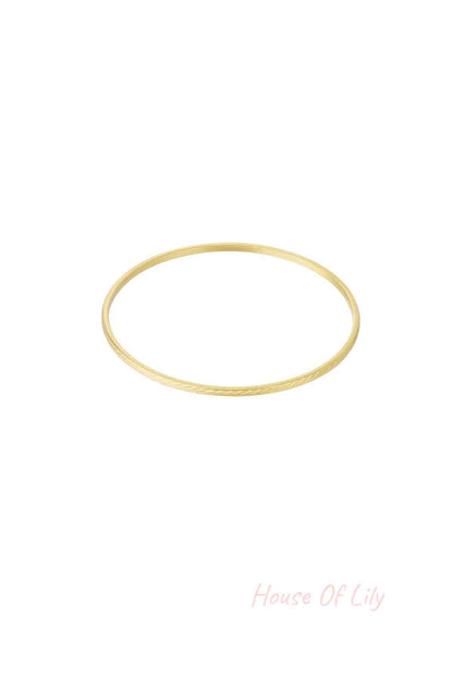 Single slim gold bangle with a delicate engraved pattern on white background