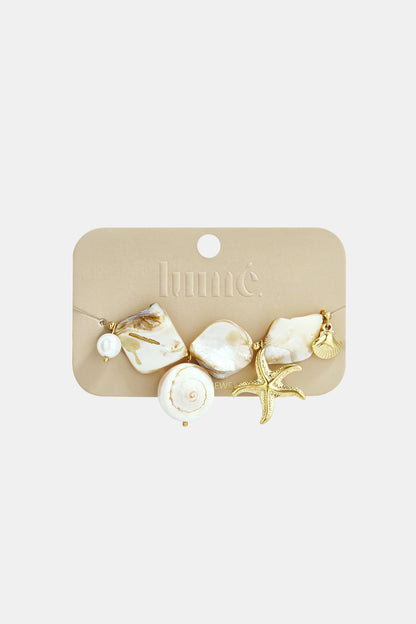 Mother Pearl Sea Charm bracelet featuring iridescent shell pieces, a gold starfish, and seashell charms on a display card.